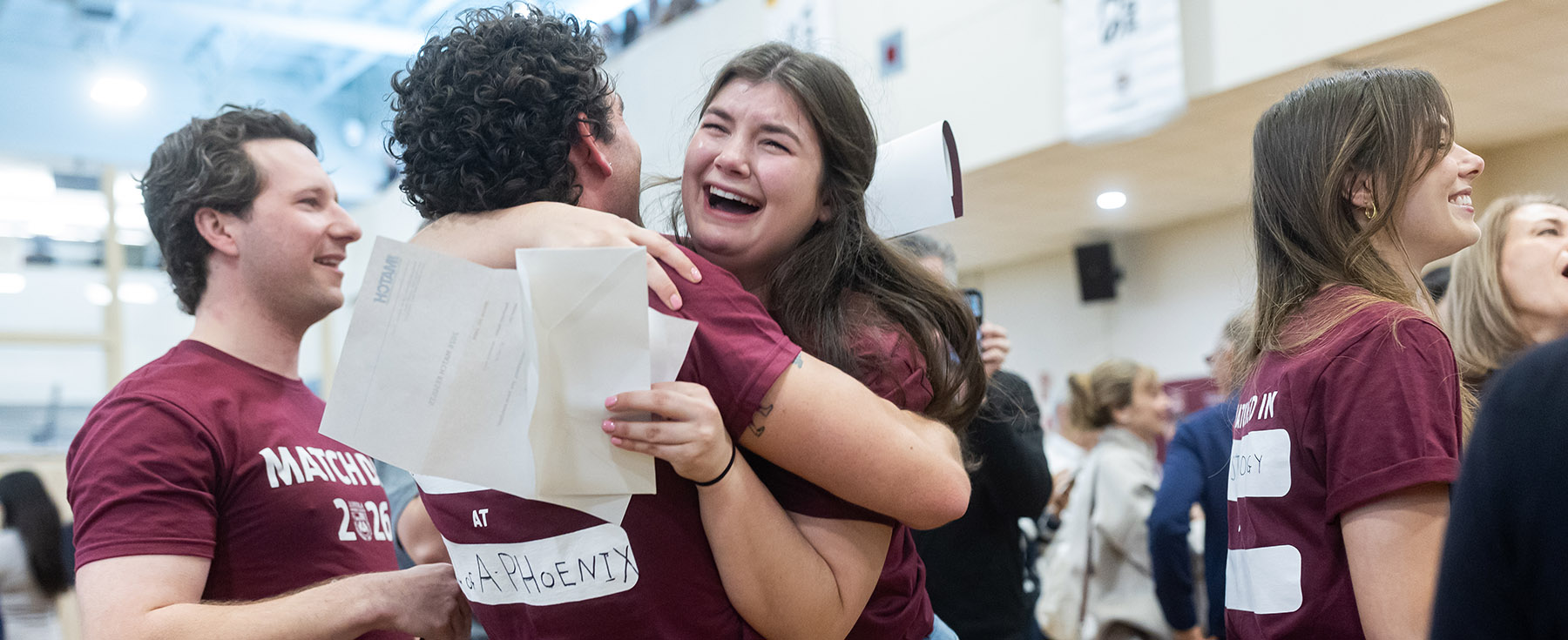 Two students wearing maroon t-shirts hug while one cries tears of joy